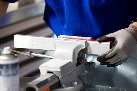 master in a blue T-shirt and gray gloves clamps a part in a vice, a worker at a workbench, close-up