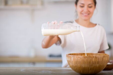 girl pouring milk from a plastic bottle into a wooden bowl, smiling in the background.の写真素材