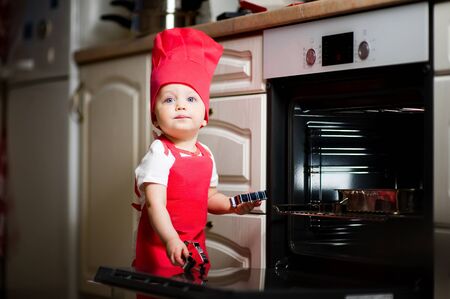 little girl in a red cook suit plays with kitchen utensils near the oven. Playing in the kitchenの写真素材