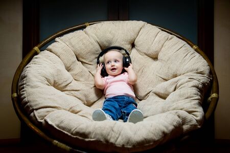 the child listens to music in large headphones while sitting in a large easy chairの写真素材