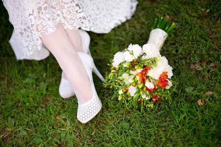 Close-up of bride's legs on the grass and a wedding bouquet lying nearby. top viewの写真素材