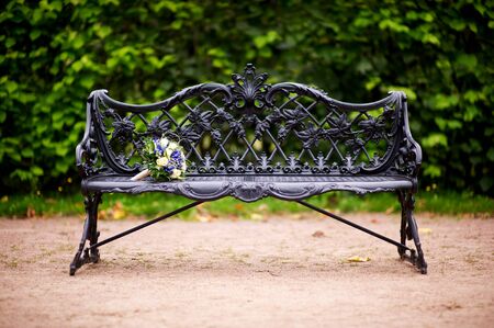 the bride s bouquet lies on the edge of an elegant cast-iron bench in the parkの写真素材