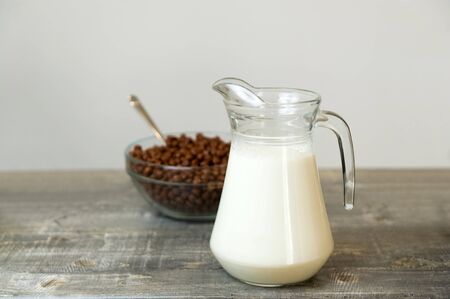 On the table is a transparent jug with fresh milk and in the background is a cup with chocolate flakes in the form of balls. Quick breakfast at the hotel.の写真素材