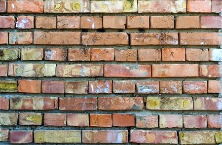 A wall of bricks, roughly laid out with heterogeneous spots and cracked paintの写真素材