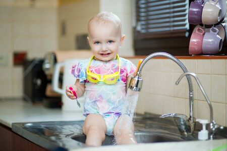 little girl in a swimsuit and swimming glasses has fun in the sink in the kitchenの写真素材