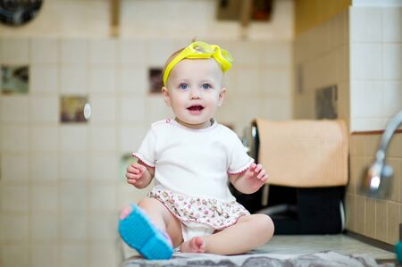 little girl with swimming goggles and one boot sits on a kitchen worktopの写真素材