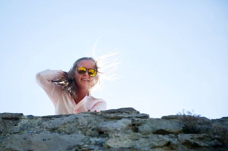a young woman with glasses looks down from the wall and smiles, while the wind rubs her hair, in the...