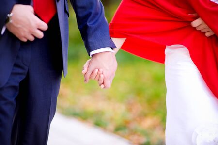 the groom in a blue suit holds the hand of the bride in a red scarf. Close-upの写真素材