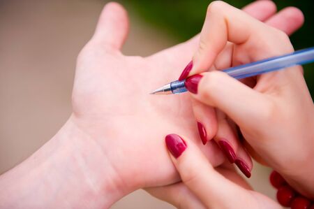 the girl is going to write to the guy on his hand her phone number with a blue pen, close upの写真素材