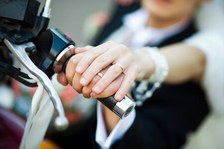 the bride s hand with a wedding ring lies on the groom s hand with a wedding ring on it. Hands of the bride and groom lie on the handle of a motorcycle symbolizing unity and rebellious spiritの写真素材