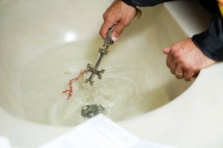 priest dips a large cross in a sink with water during the rite. close upの写真素材