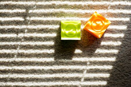 two colored childrens cubes lie on the floor, they are illuminated by the light from the window...
