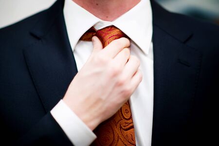 close-up of a man in a jacket and shirt straightens his tie