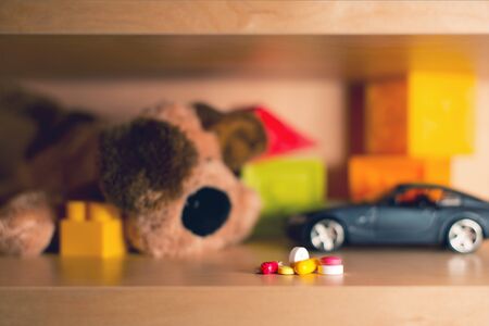 a bunch of multi-colored pills on the background of blurry children's toys. Painful childhood conceptの写真素材