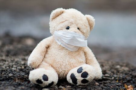 A teddy bear in a protective medical bandage sits on dirty soil, symbolizing a dangerous habitat,...