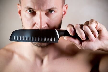stern man closes his mouth with a kitchen knife and looks angryの写真素材
