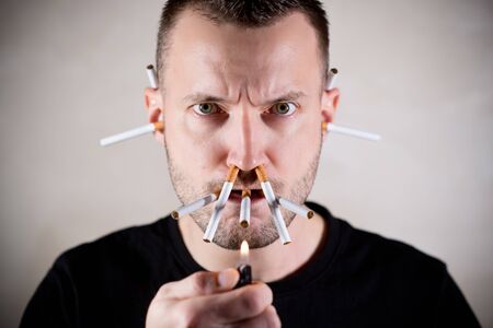 unshaven man sternly looks into the camera, intending to light a lot of cigarettes at once, which...