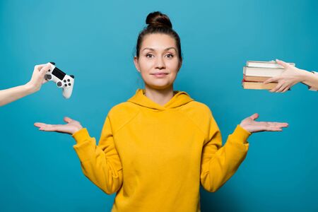 A bright girl in a yellow sweatshirt on a blue background shows with her hands the choice between...