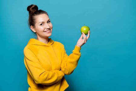 smiling girl in a bright sweatshirt holds an apple in her handの写真素材