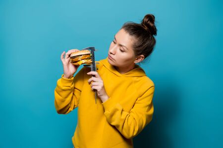 bright girl in a sweatshirt diligently measures the height of the burger with a caliperの写真素材