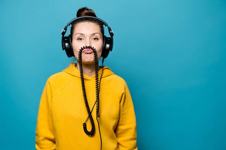 The girl in the big headphones is fooling around, holding the wire from the headphones between her...
