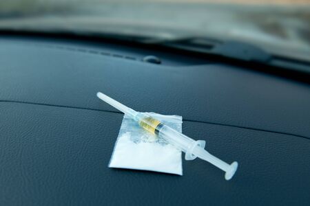 a syringe and a bag with a dose of the drug lie on the dashboard of the car, close upの写真素材