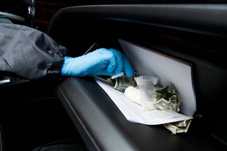 gloved police officer inspects and finds drugs in the detainee's glove compartment, no face