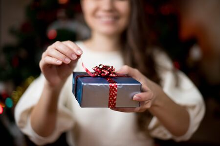 a young woman opens a gift that she holds in her hands. Close-up, focus on the giftの写真素材