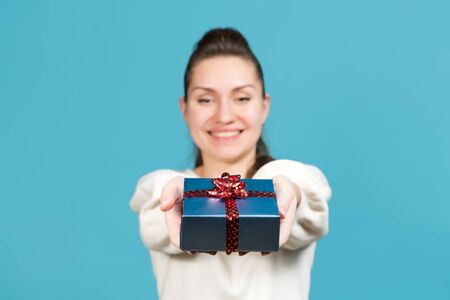 girl holds out a small gift. Selective focus on the gift. Blue background, studio