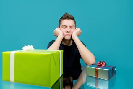 a teenager is upset looking at a small gift, next to which lies a large. Blue backgroundの写真素材