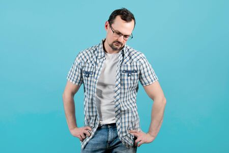 a man in a plaid shirt with bristles in glasses stands in a very relaxed position and looks down. He is very tiredの写真素材