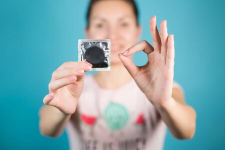 A young girl holds a condom in one hand, with the other hand shows an ok sign with her fingers....