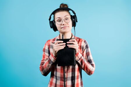 Cute calm girl in big headphones whose plug is inserted into a paper book. A girl holds a book in...
