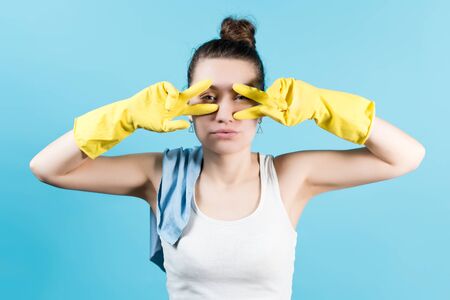 Young woman in a T-shirt fooling around and posing in yellow household gloves. Isolated on blueの写真素材