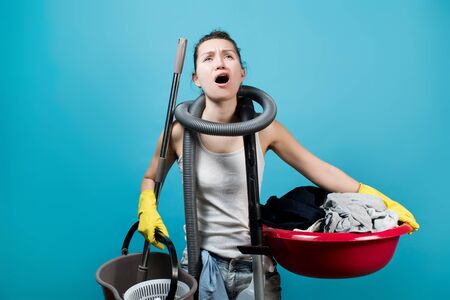 A suffering housewife keeps everything on herself - a vacuum cleaner, a mop with a bucket and a basin with dirty laundryの写真素材