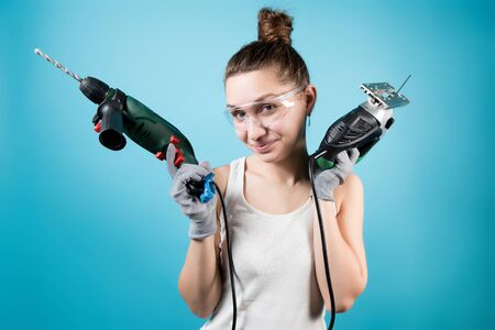 Young woman and men's power tools - jigsaw and electric drill. Isolated on blue