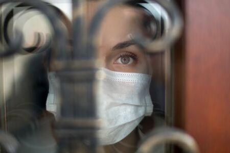 Cold look of a girl through the front door of a house during quarantine and self-isolationの写真素材
