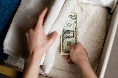 a hand takes or puts a small stack of crumpled dollar bills in a towel box. Poor savings