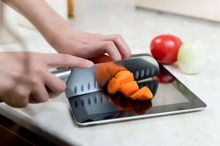 A woman cuts vegetables with a knife on an old graphics tablet, which serves as a cutting board