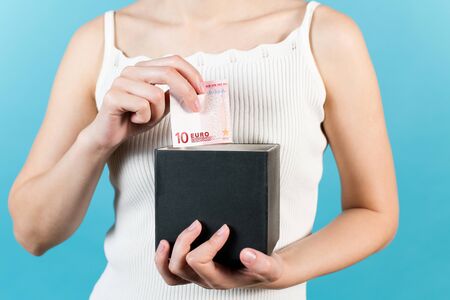 A girl takes out or puts ten euros into a savings box. Close-up without a face