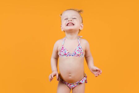 girl in a swimsuit smiles in all teeth, funny squinting eyes. Isolated on yellow-orange backgroundの写真素材