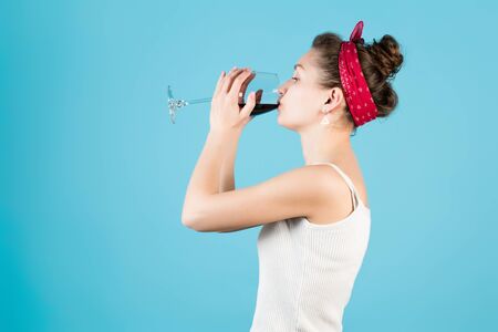 girl holds a glass of wine with two hands and drinks on a blue backgroundの写真素材