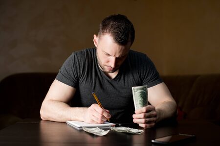 A man with a serious face counts the remaining funds and plans expenses. Financial difficulties, lack of moneyの写真素材