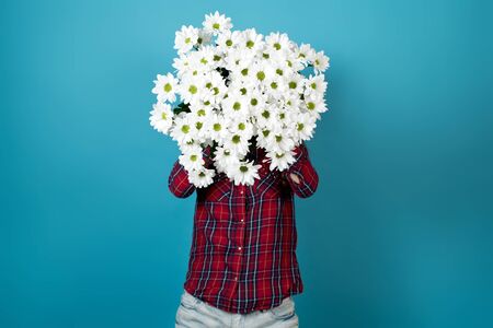 A girl in a red checkered shirt holds in front of him a bouquet of white chrysanthemums on a blue backgroundの写真素材