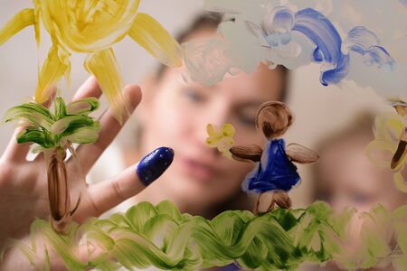 Mom teaches a child to draw by sliding her daughter s fingers on glass and dipping in paint. Selective focusの写真素材
