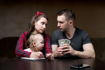 Counting family money. Husband and wife look at each other seriously, a little daughter sits on his...