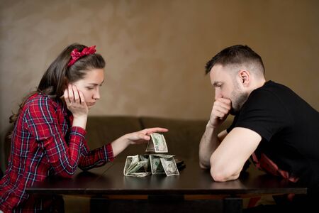 Husband and wife are sadly looking at the remaining money, sitting at a table in the kitchen. Difficult financial time in a young familyの写真素材