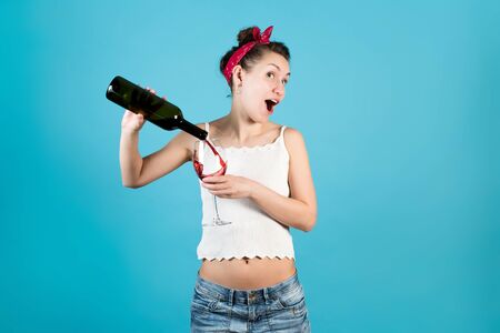 Cheerful bright girl pours the rest of the wine into a large glass on a blue backgroundの写真素材