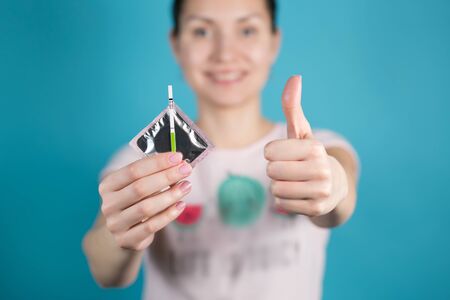 A young girl holds out a condom and a negative pregnancy test into the camera, the second hand shows a thumb upの写真素材