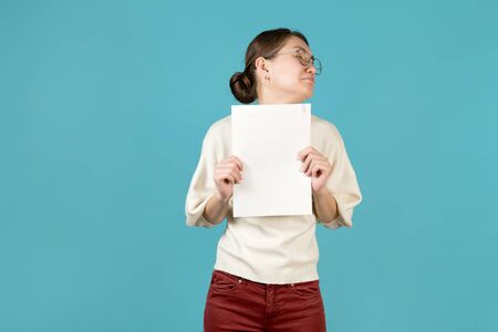 Young upset woman with documents in her hands turns away from something, blue backgroundの写真素材